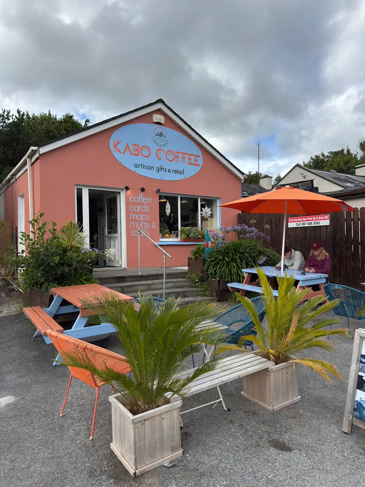 Kabo Coffee exterior with outdoor seating, coral building and palm planters in Letterfrack village